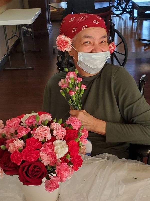 An older adult arranging pink and red flowers in a vase. Next Avenue, benefits of flowers, mind and body