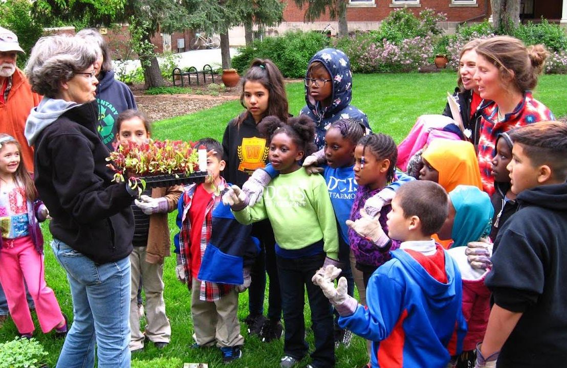 A group of young people gathered around an older adult showing off small seedlings. Next Avenue, Gardening exercise