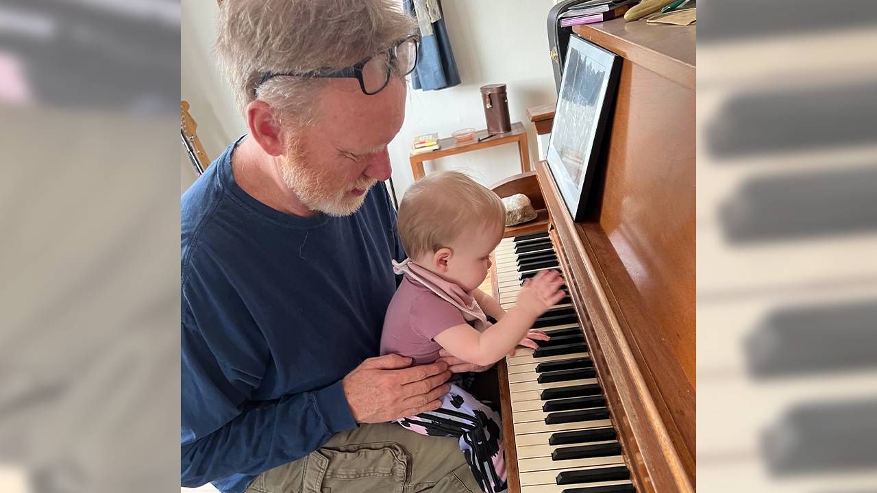 A grandparent with his granchild on his lap playing the piano. Next Avenue, grandparenting, grandparents child care