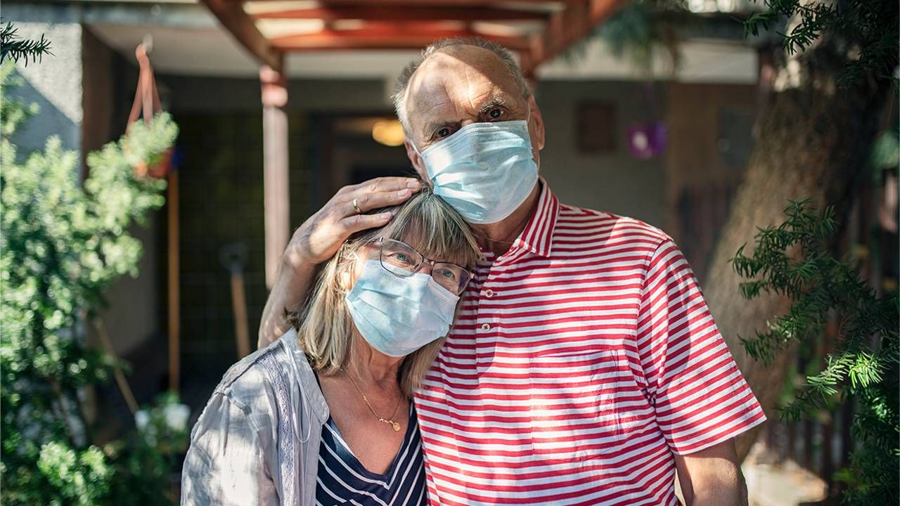 A couple standing outside their house wearing facemasks. Next Avenue, returning to normal, Immunocompromised, pandemic