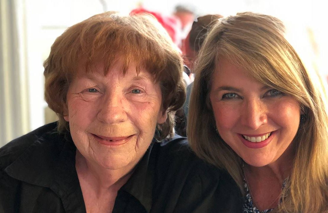 An older adult and her adult child smiling together while sitting outside. Next Avenue, resources for dementia caregivers