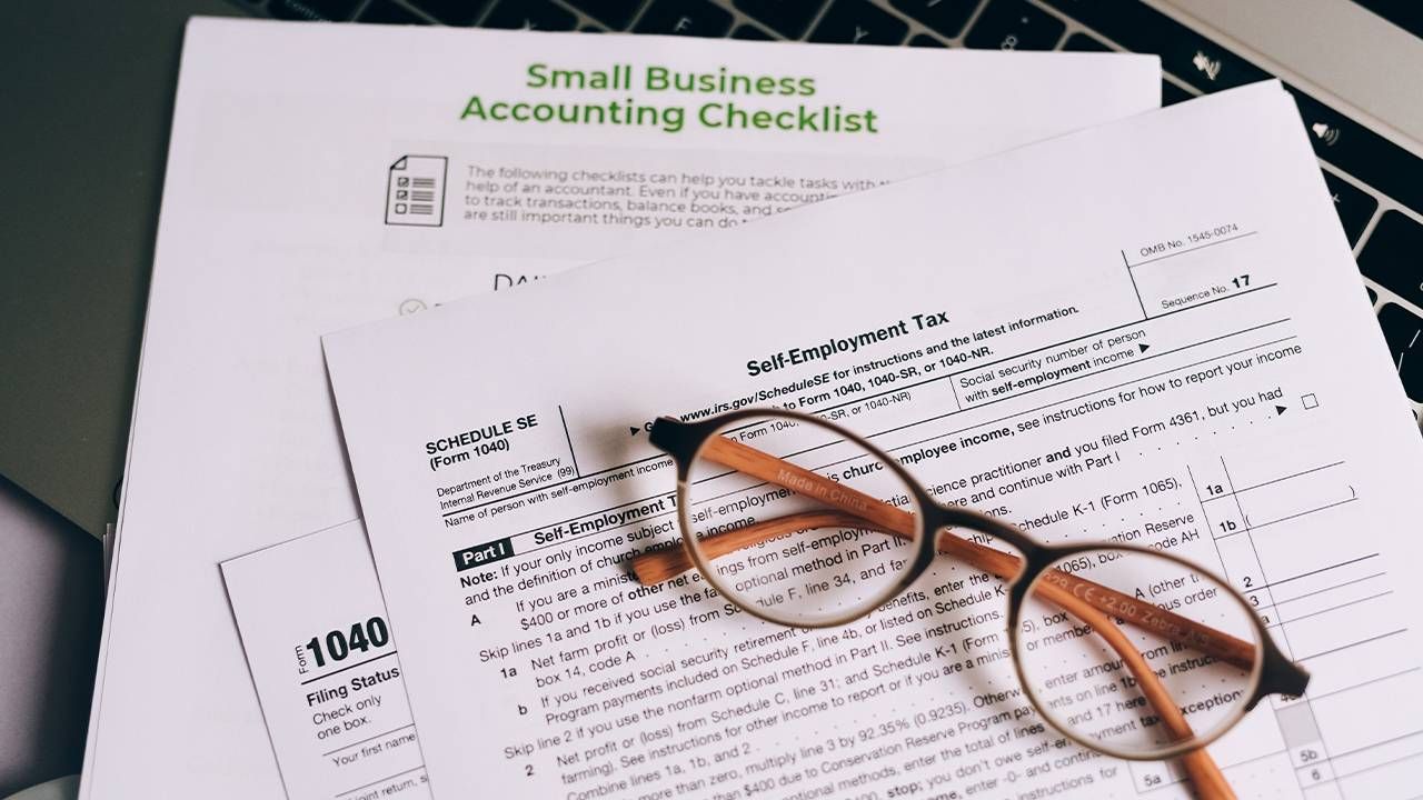 Tax documents on top of a laptop computer. Next Avenue, entrepreneur, small business taxes