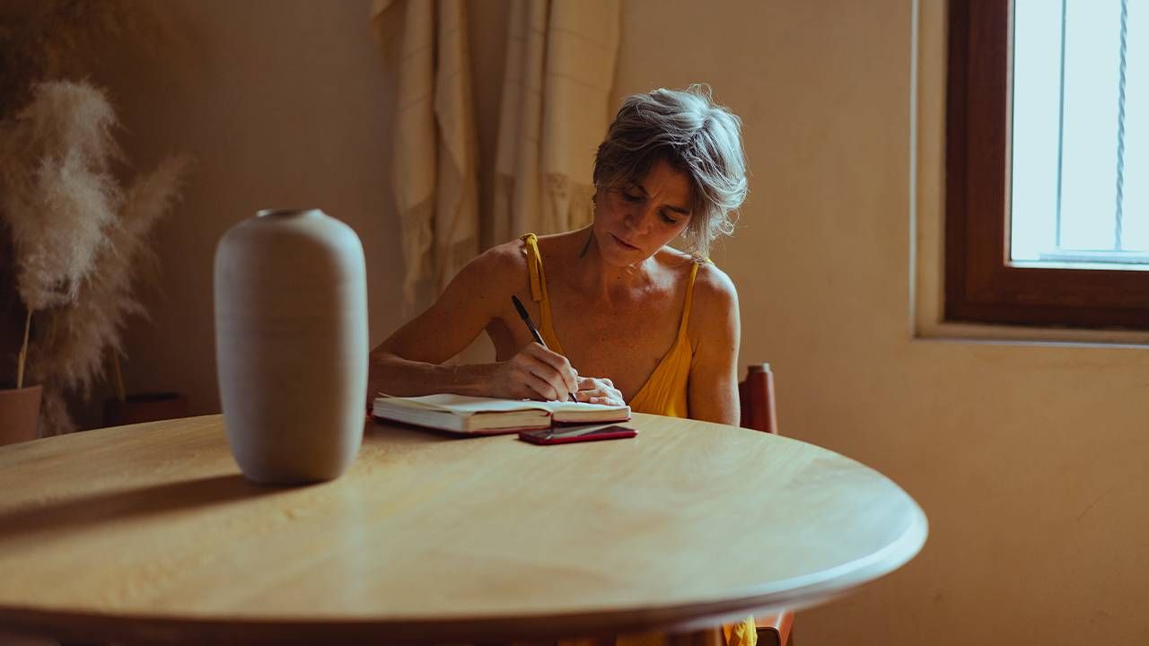 An older adult sitting at a table writing in a diary or journal, what to do with old journals or diaries. Next Avenue, how to destroy old diaries