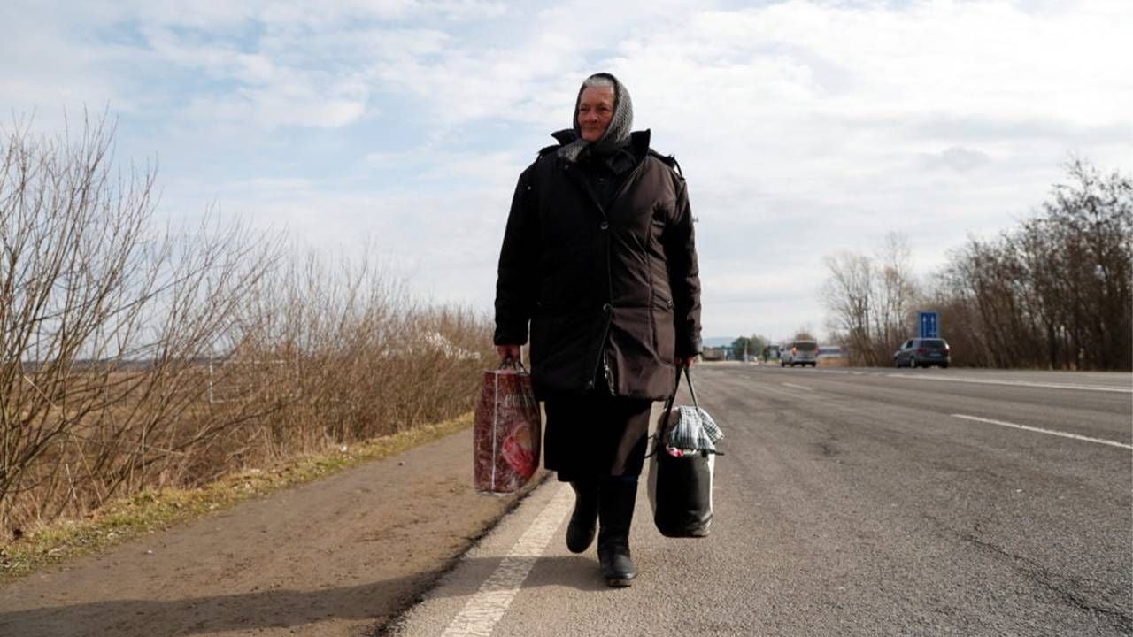 A woman walking on the side of the road holding suitcases. Next Avenue, Russian Ukrainian elders