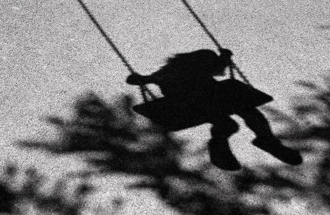 A black and white photo of a silhouette of a schoolgirl on a swing. Next Avenue, childhood bully, adults deal with childhood trauma