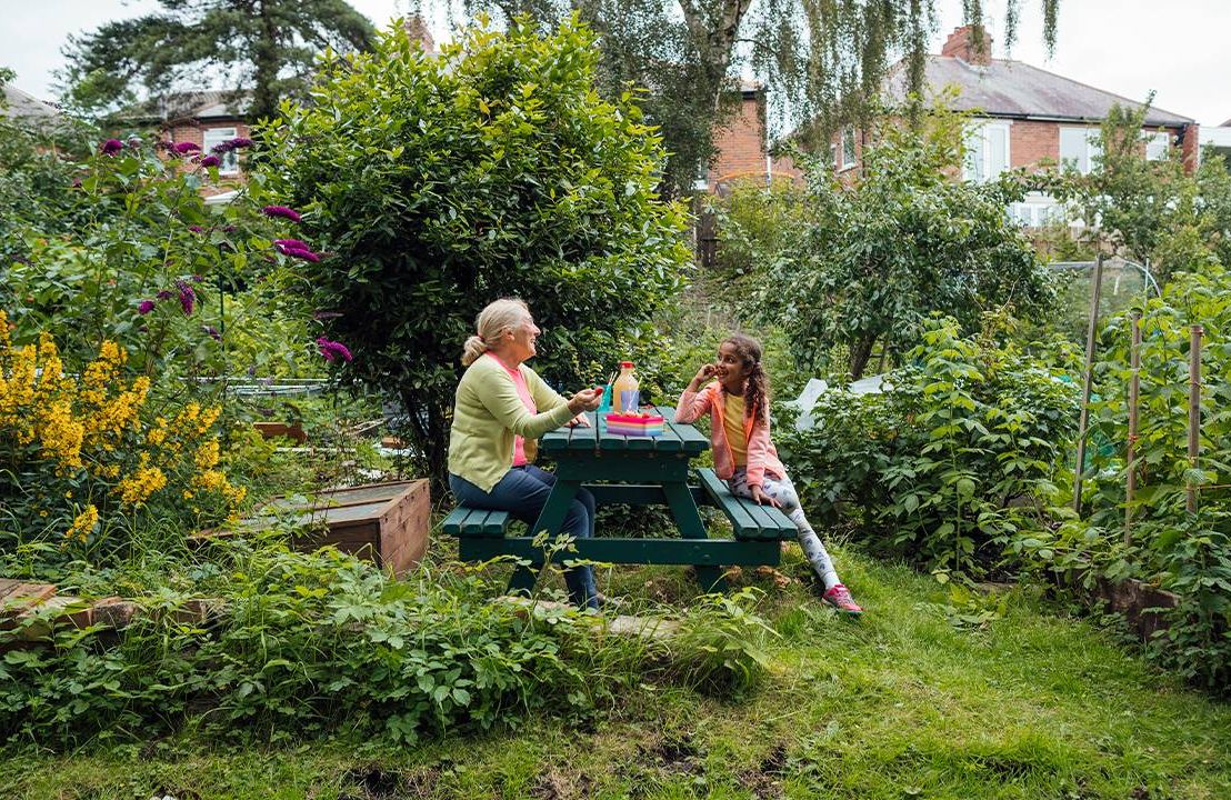 A grandmother eating gluten free food with her granddaughter on a picnic table. Next Avenue, celiac disease help