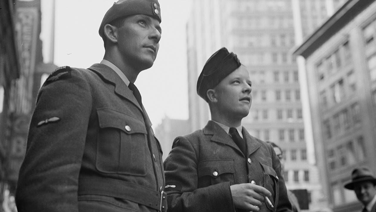 A black and white photo of two men wearing military garb looking up toward a building. Next Avenue, Vietnam Vets, WWII vets, memorial day, greatest generation