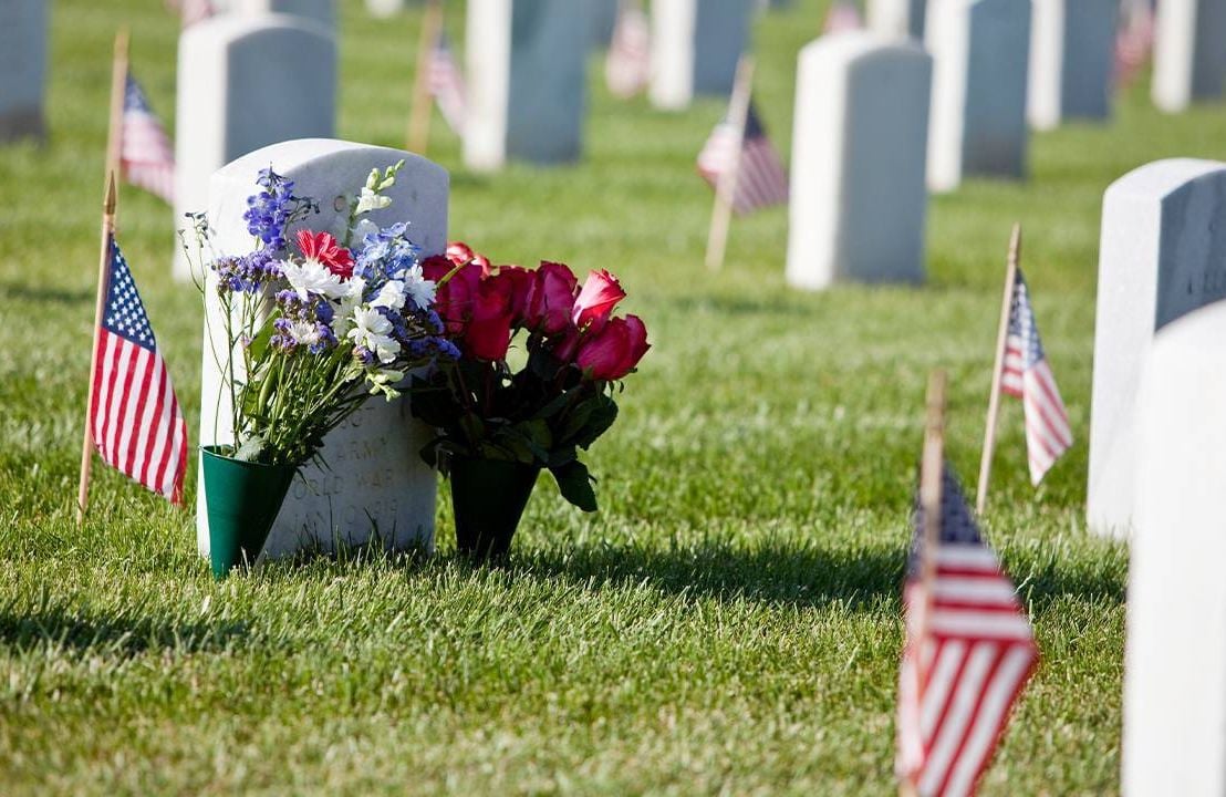 Flowers and an American flag on a veteran's gravestone. Next Avenue, memorial day