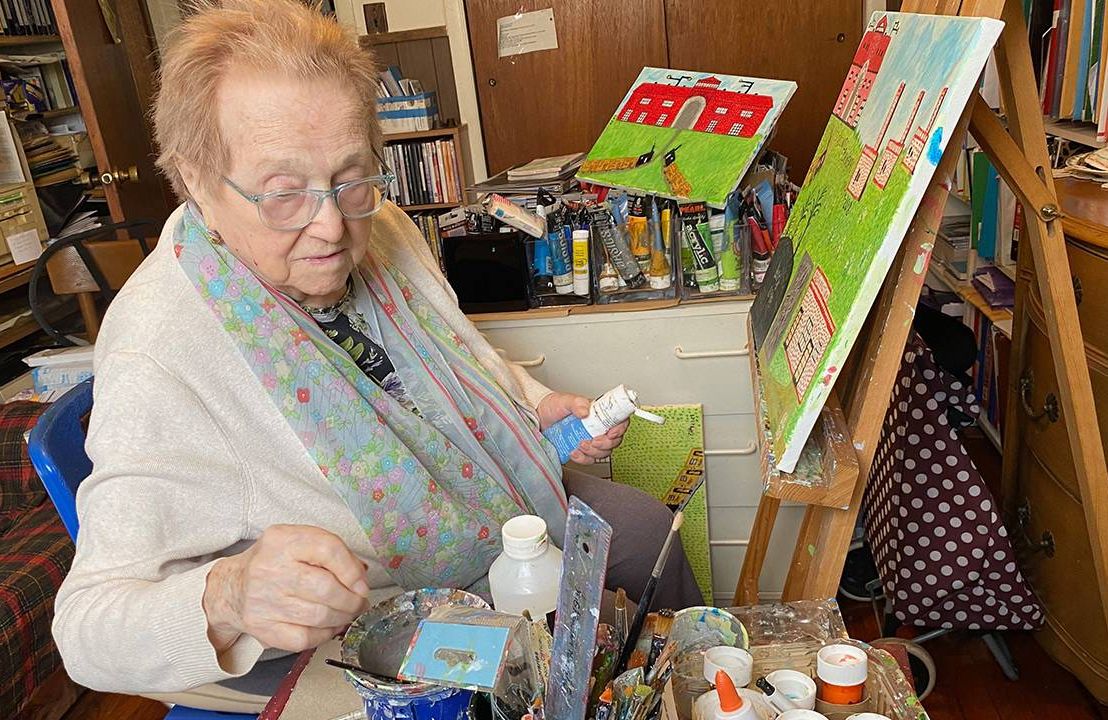An older woman sitting in front of an easel while painting. Next Avenue, holocaust survivor story