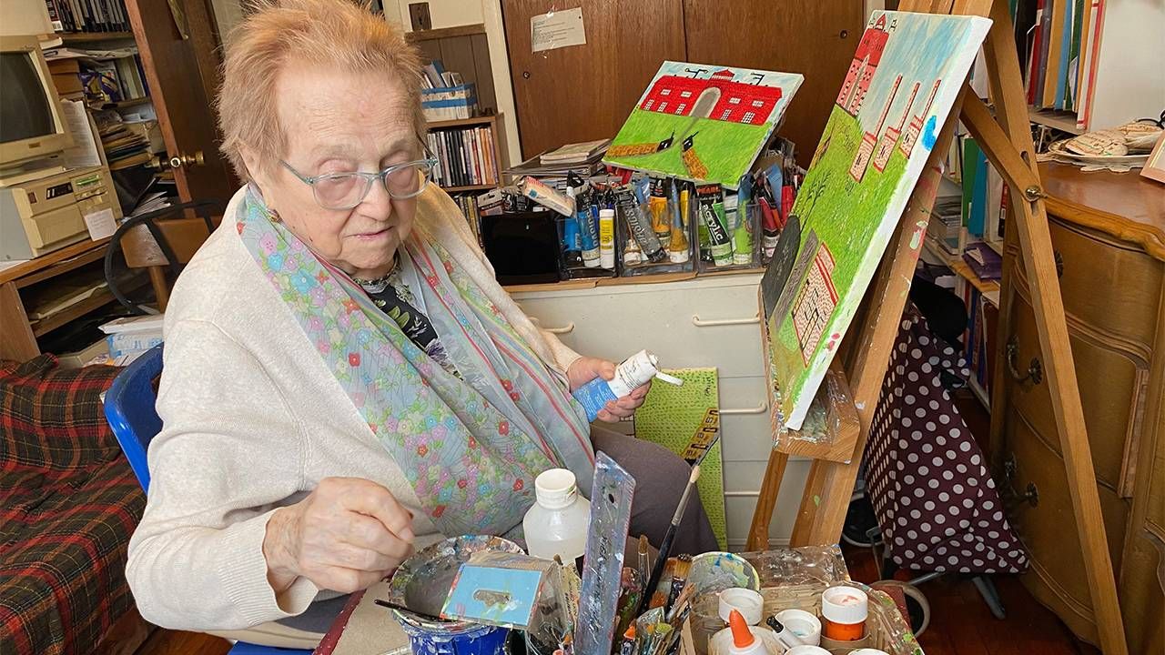 An older woman sitting in front of an easel while painting. Next Avenue, holocaust survivor story