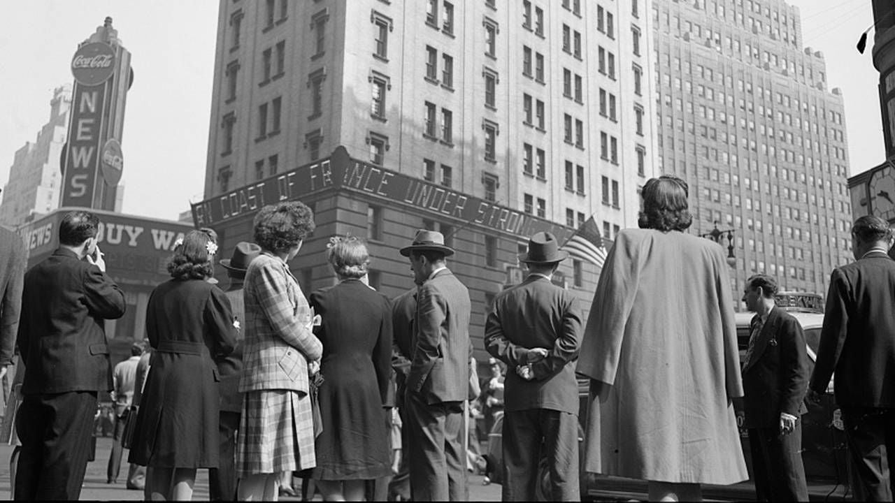 A crowd of people gathered in Times Square looking up at a building. Next Avenue, Vietnam Vets, WWII vets, memorial day, greatest generation