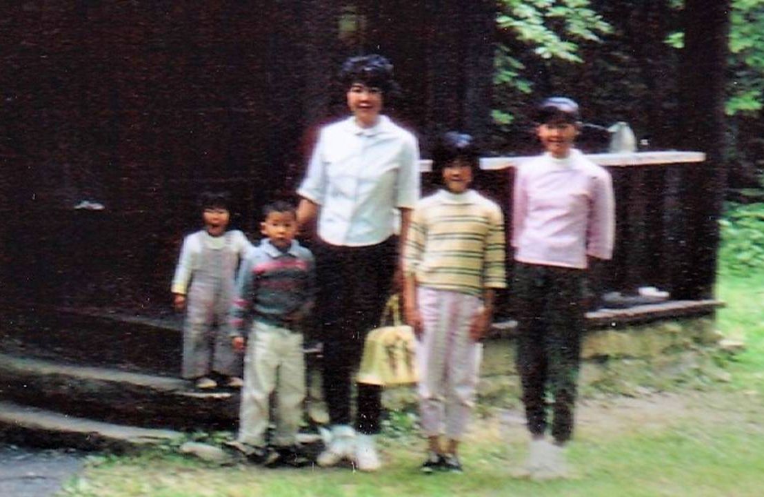 An old photo of a family standing outside a cabin. Next Avenue, family road trip