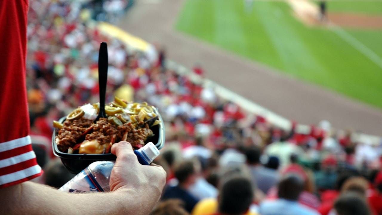 A man holding a plate full of nachos in the stadium of a baseball game. Next Avenue, are hotdogs healthy