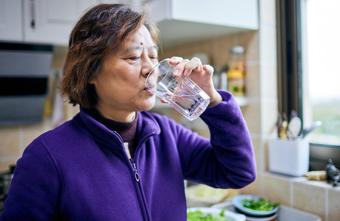 An older adult drinking a glass of water at home. Next Avenue, is sparkling water hydrating