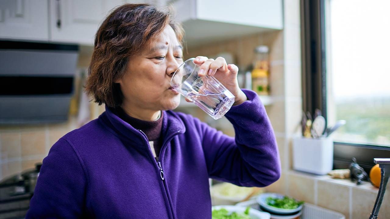 An older adult drinking a glass of water at home. Next Avenue, is sparkling water hydrating