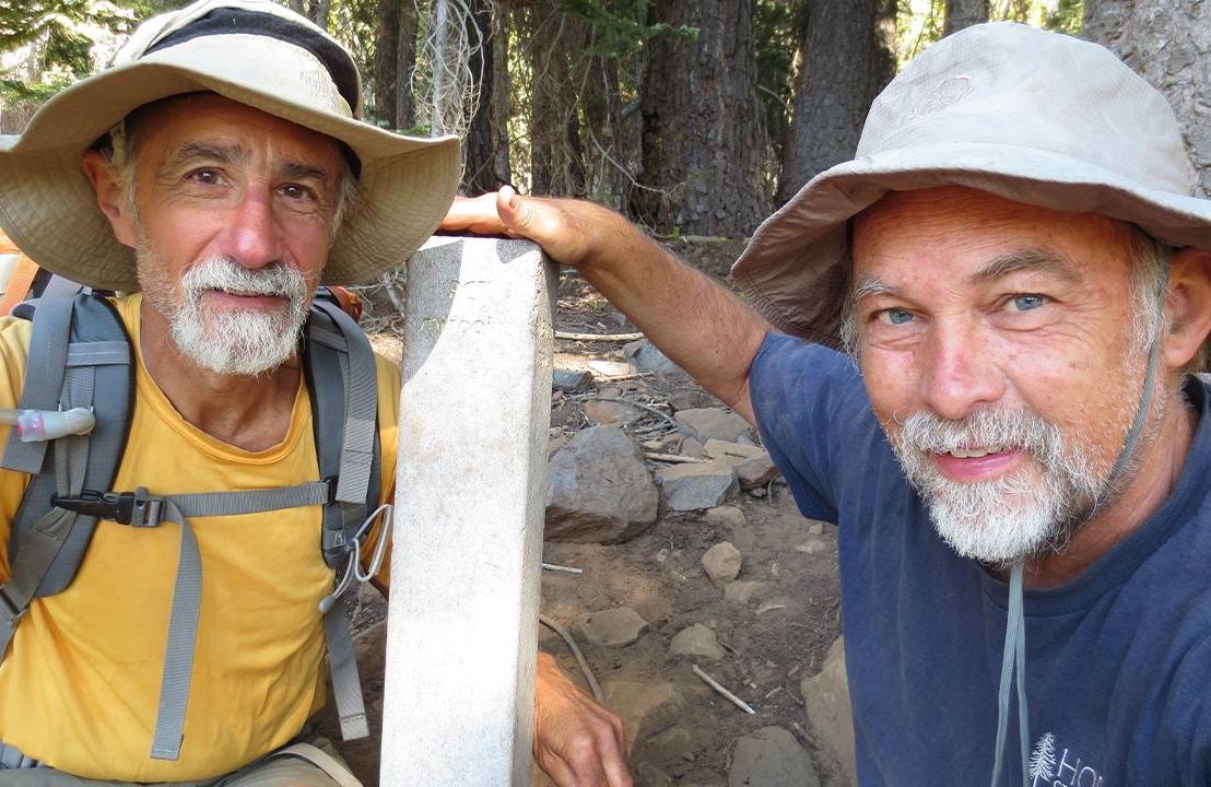 Two older adults crouching down next to a mile marker on the Pacific Crest Trail. Next Avenue, Pacific Crest Trail section hike