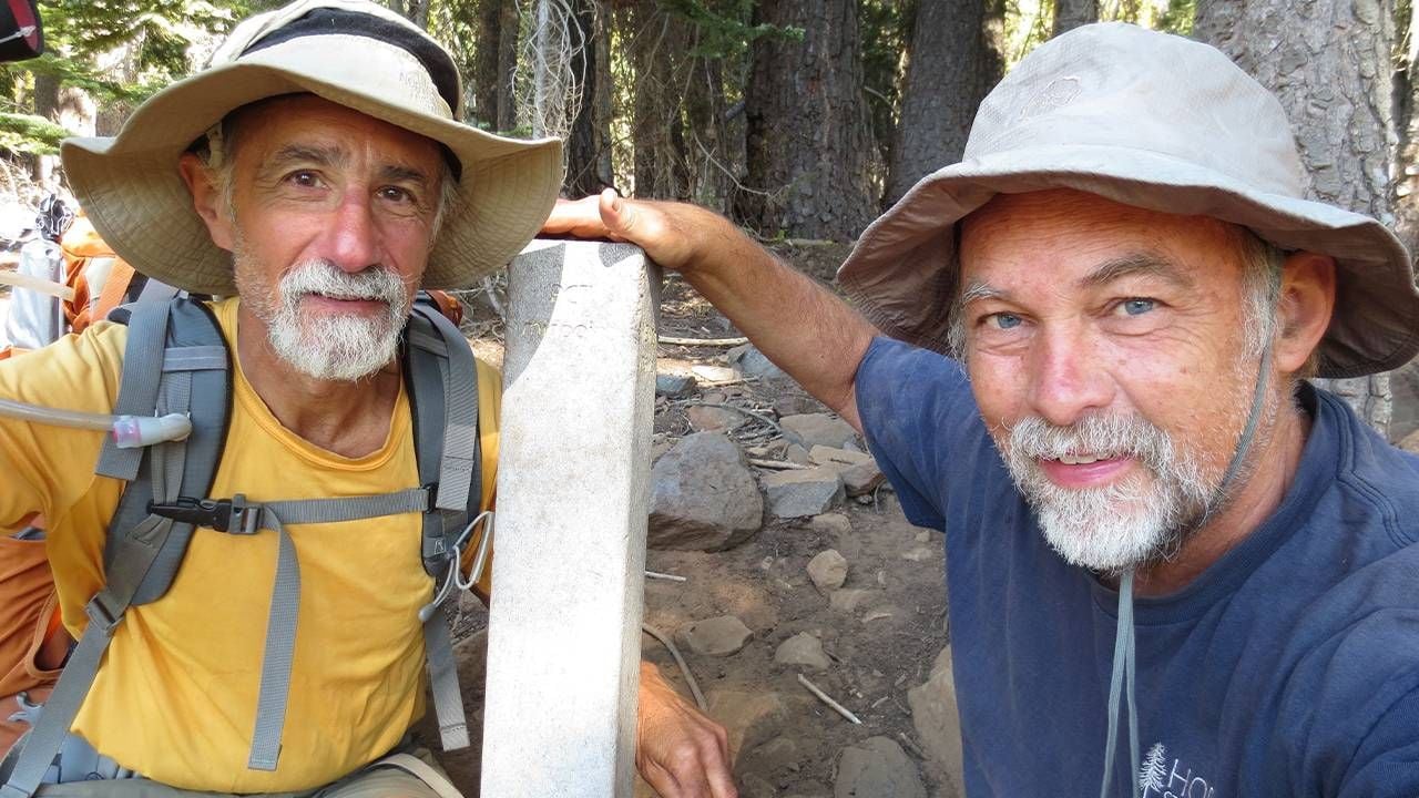 Two older adults crouching down next to a mile marker on the Pacific Crest Trail. Next Avenue, Pacific Crest Trail section hike