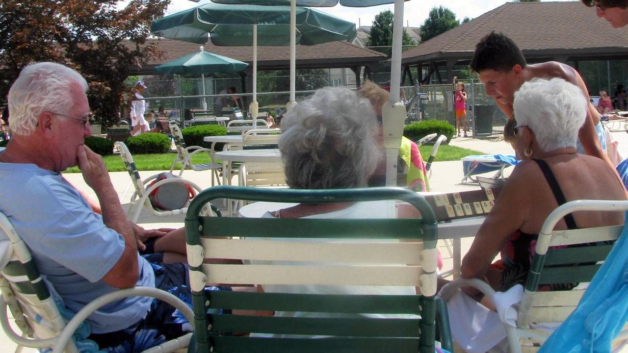 A group of older adults sitting at a poolside table playing rummikub. Next Avenue, age gap friendship, intergenerational friendship