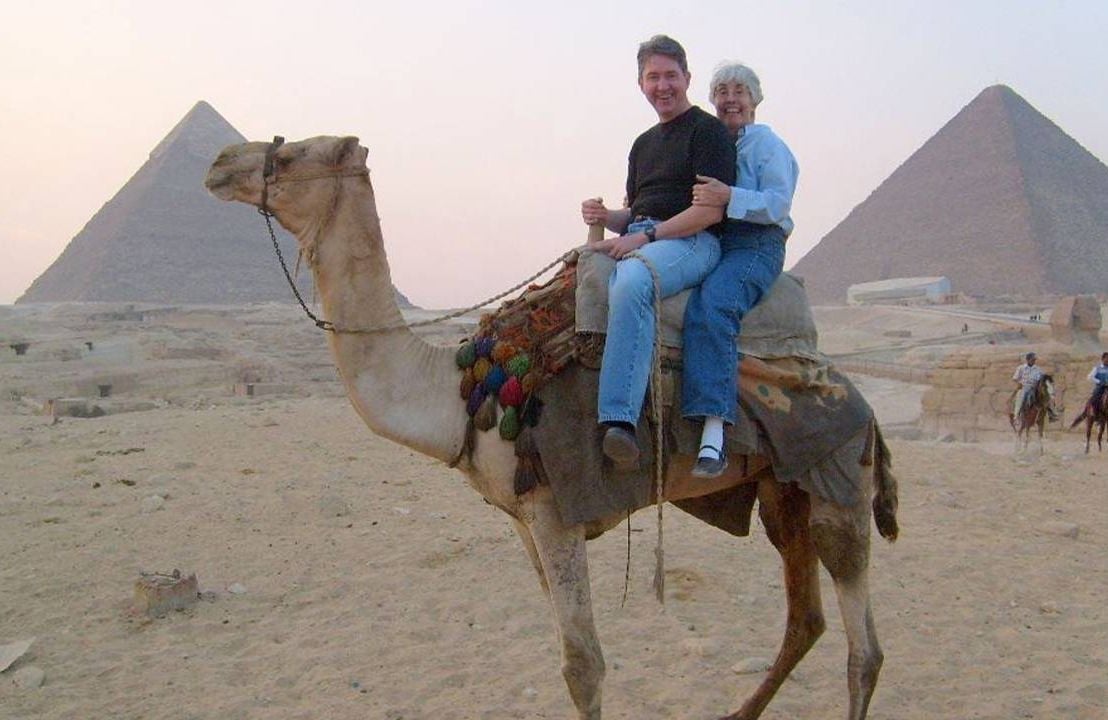 Two older adults riding a camel with Egyptian Pyramids in the background. Next Avenue, dementia resources caregivers