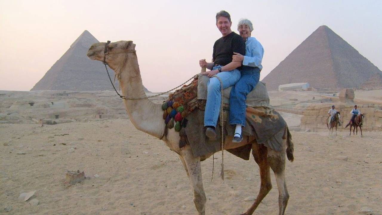 Two older adults riding a camel with Egyptian Pyramids in the background. Next Avenue, dementia resources caregivers