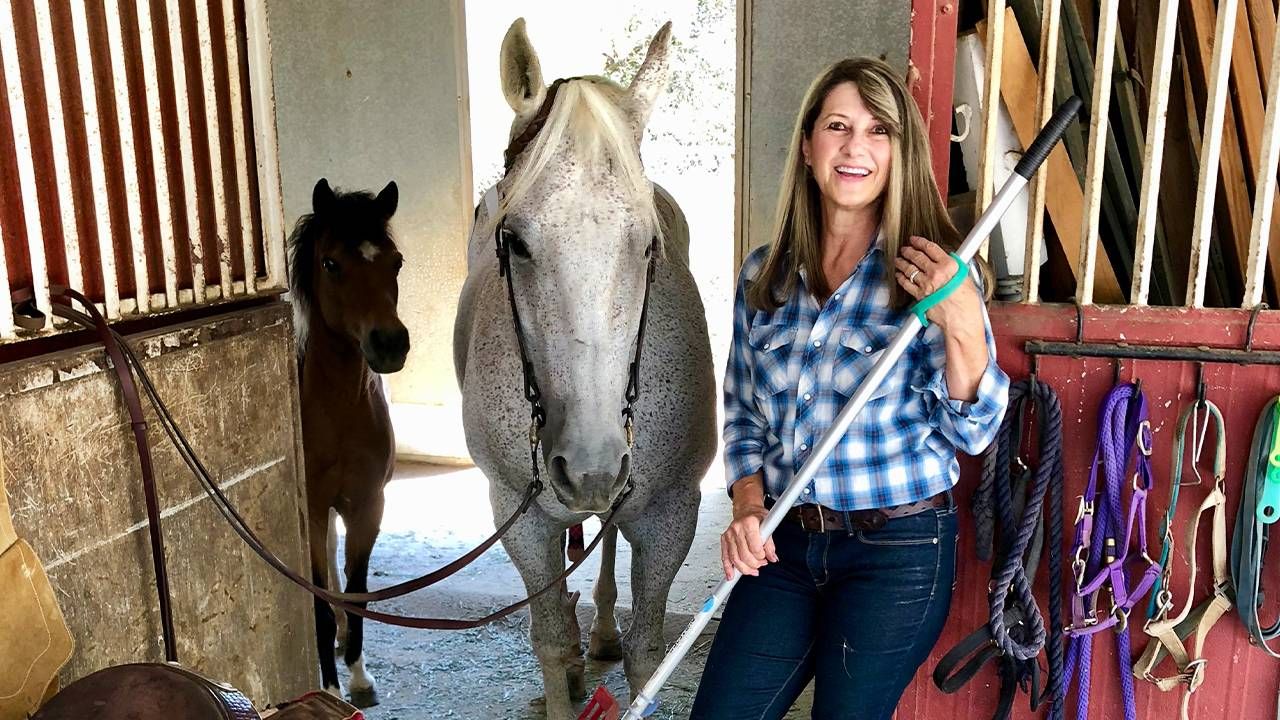 A woman smiling in a barn while holding a rake. Next Avenue, career shift stories