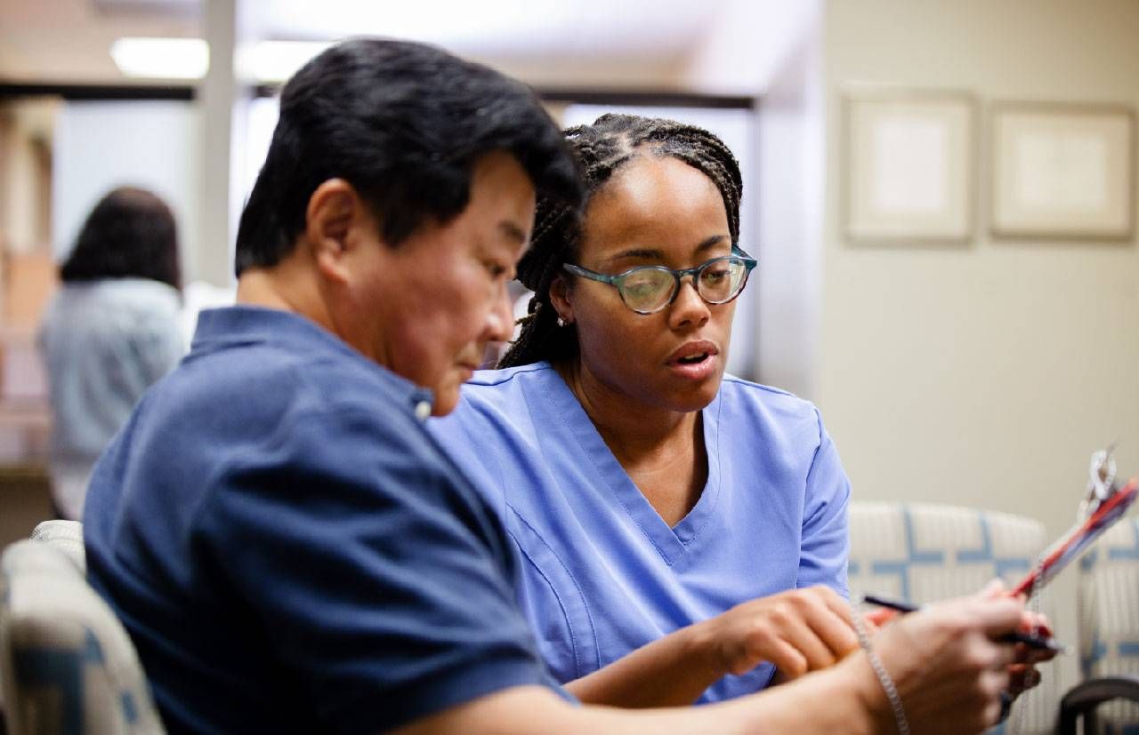 A man filling out paperwork with a nurse in the doctor's office waiting room. Next Avenue, unnecessary doctor's appointments