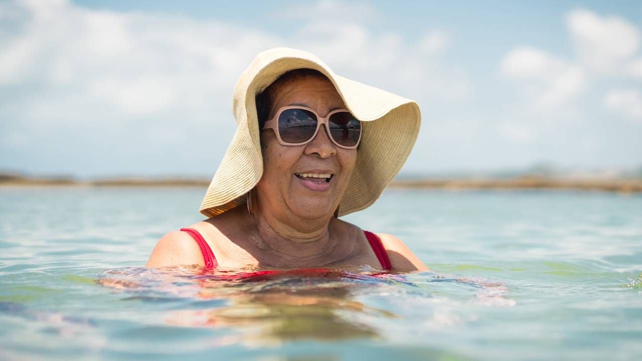 A woman wearing a sunhat while wading in the ocean. Next Avenue, skin cancer prevention