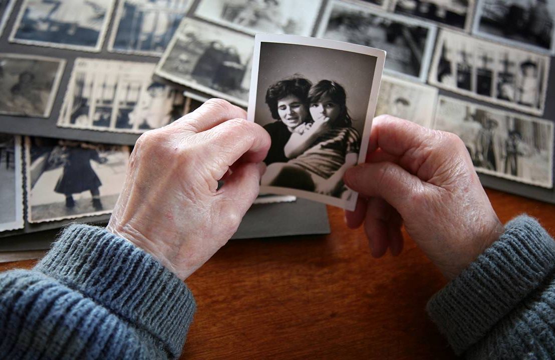 A close-up of a person's hands holding old family photos. Next Avenue, forgiving your parents