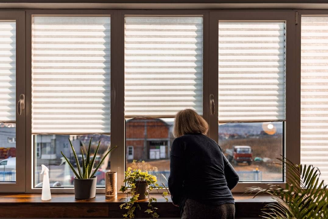 An older woman looking out the window of her apartment. Next Avenue, can't afford rent, fixed income, retirement