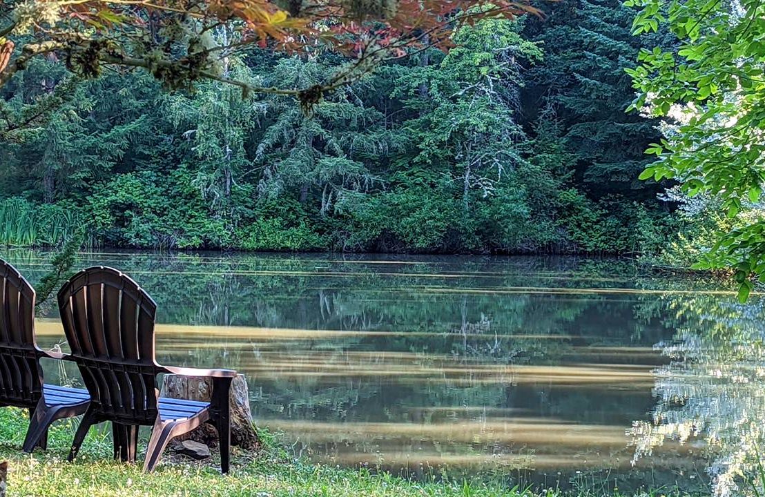 Two Adirondack chairs next to a pond in a forested area. Next Avenue, benefits of spiritual retreats