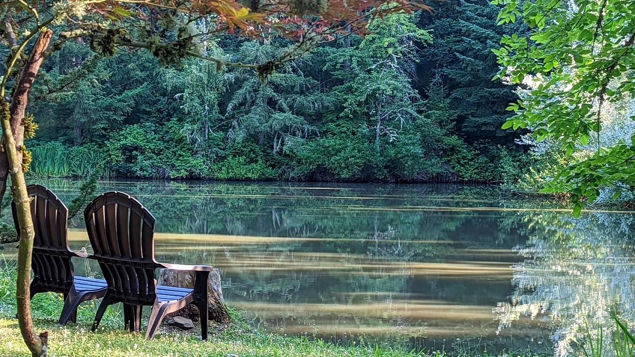 Two Adirondack chairs next to a pond in a forested area. Next Avenue, benefits of spiritual retreats
