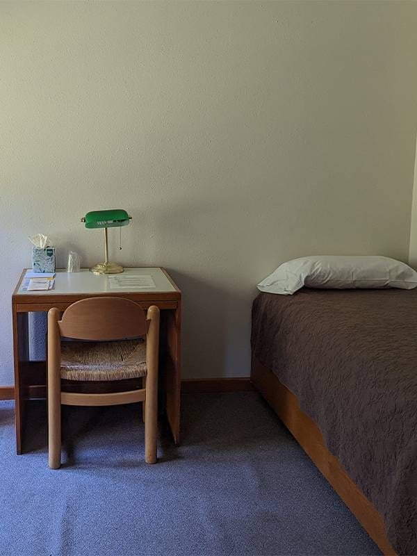 A small desk next to a twin sized bed. Next Avenue, benefits of spiritual retreats