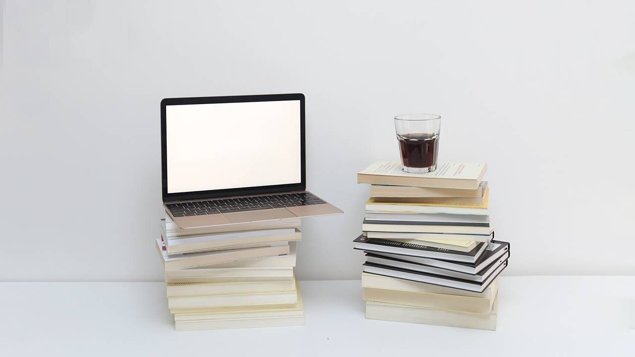 A laptop and cup of coffee on top of a stack of books. Next Avenue, how to self publish book.