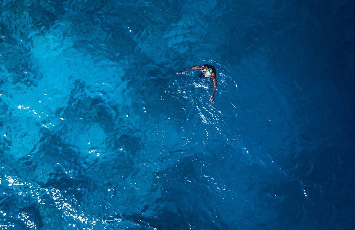 An aerial view of a swimmer in deep blue water. Next Avenue, coping with mother's death