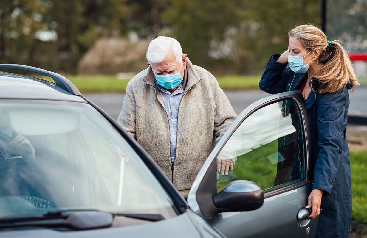 A woman caregiver helping her father into the car. Next Avenue, caring for an older parent