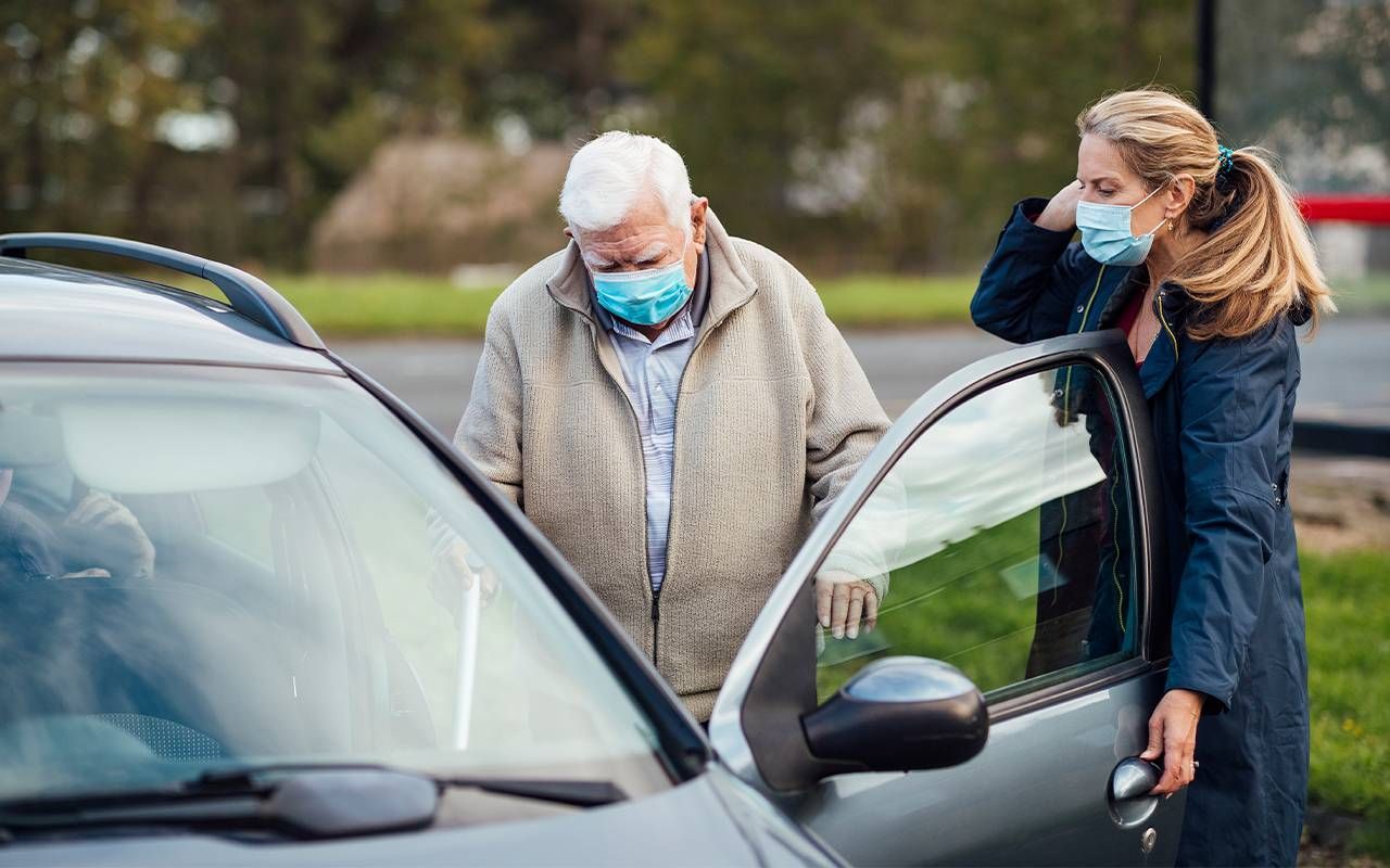 A woman caregiver helping her father into the car. Next Avenue, caring for an older parent