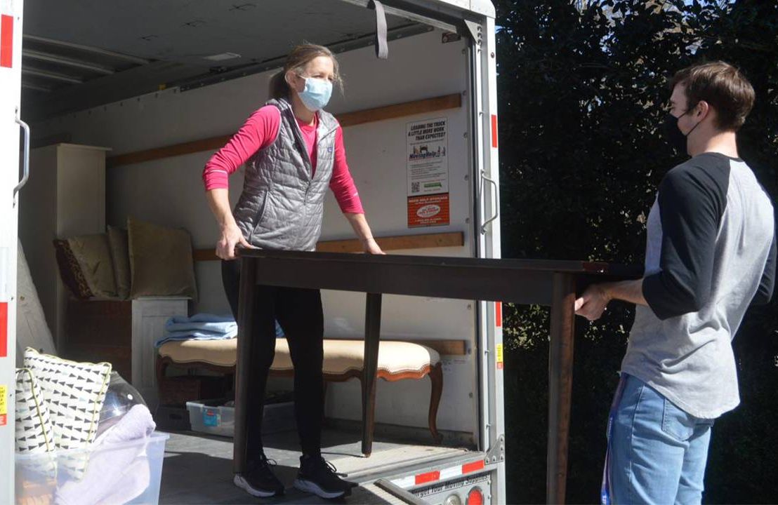 Two people carrying furniture out of a moving truck. Next Avenue, how to prevent and end homelessness among older adults