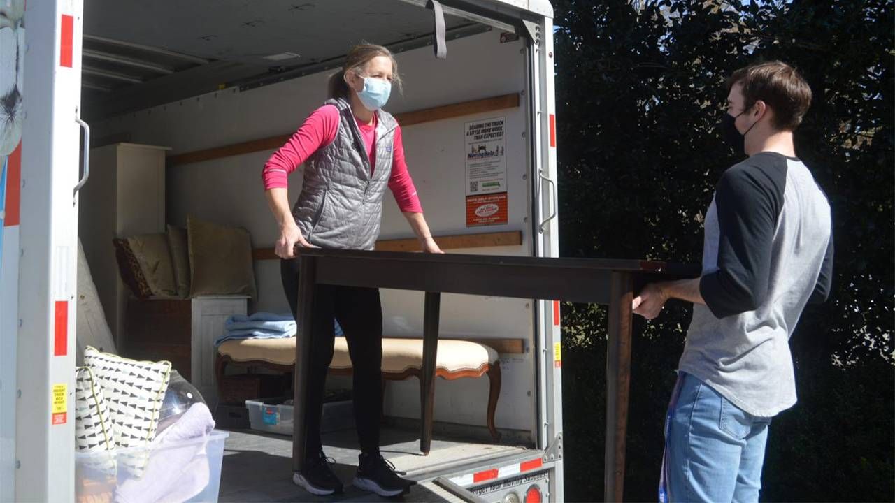 Two people carrying furniture out of a moving truck. Next Avenue, how to prevent and end homelessness among older adults
