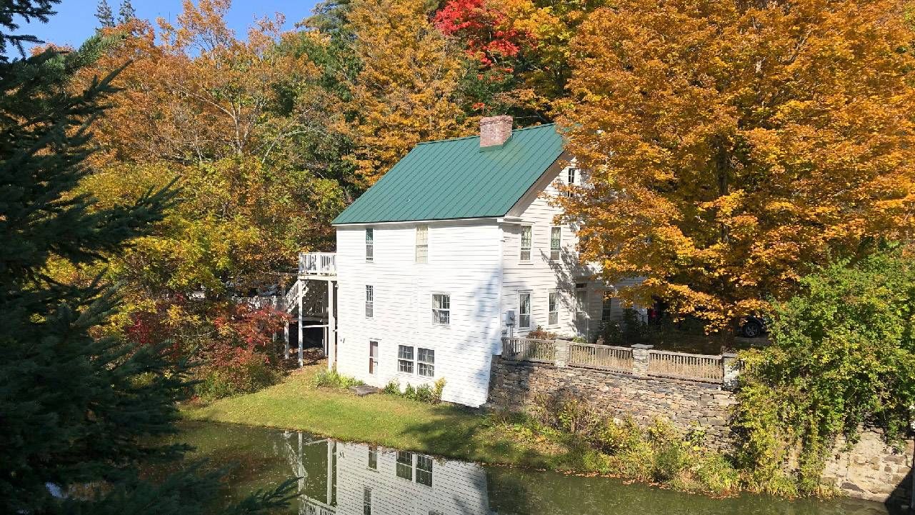 A white cabin surrounded by a forest with fall colored leaves. Next Avenue, leaf peeping, peak fall colors