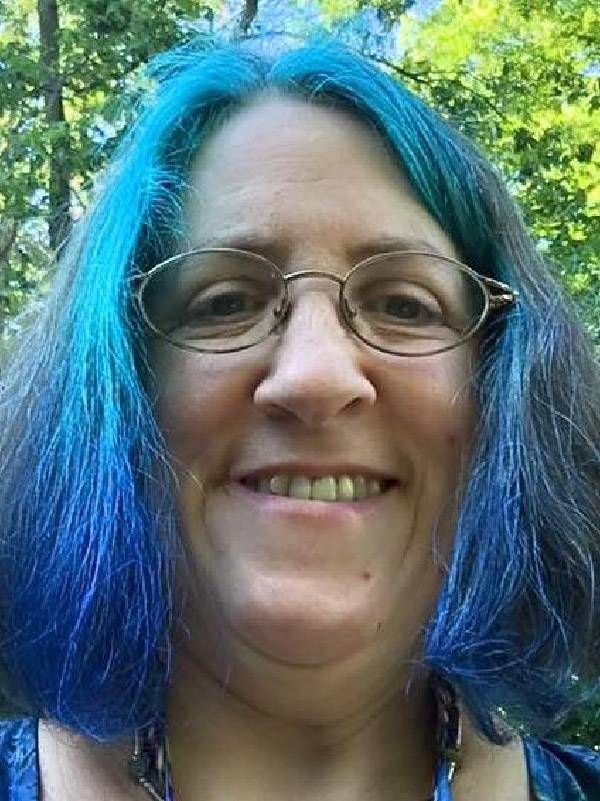 A woman with bright blue hair smiling. Next Avenue, long haul covid disability