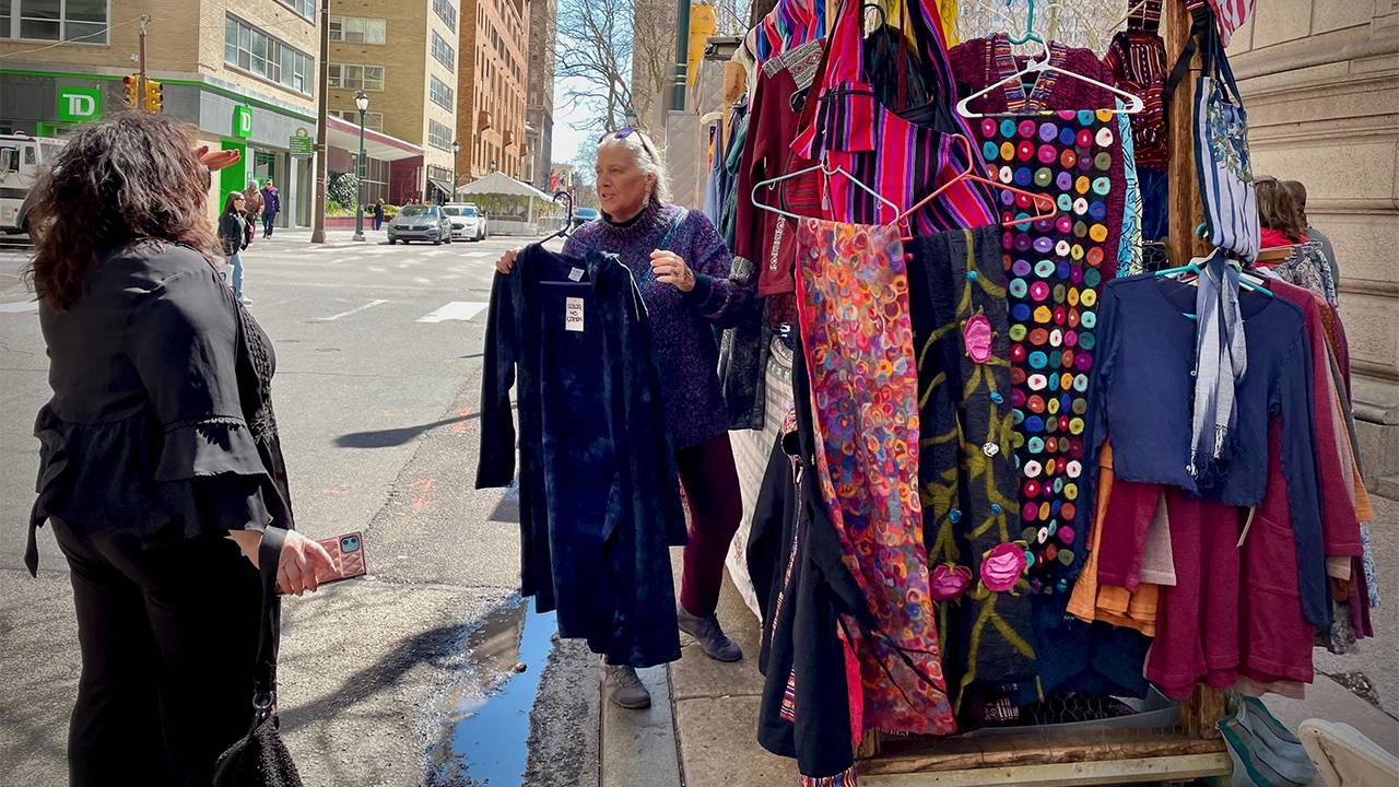 A woman selling colorful textiles on a street stand. Next Avenue