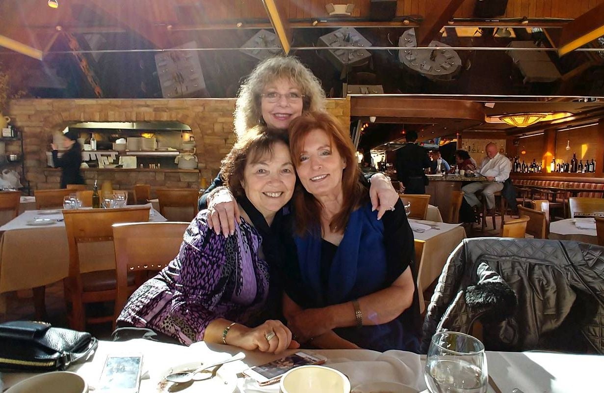 Three women with their arms wrapped around each other at a restaurant. Next Avenue, Friendship group dynamics, long lasting friendships