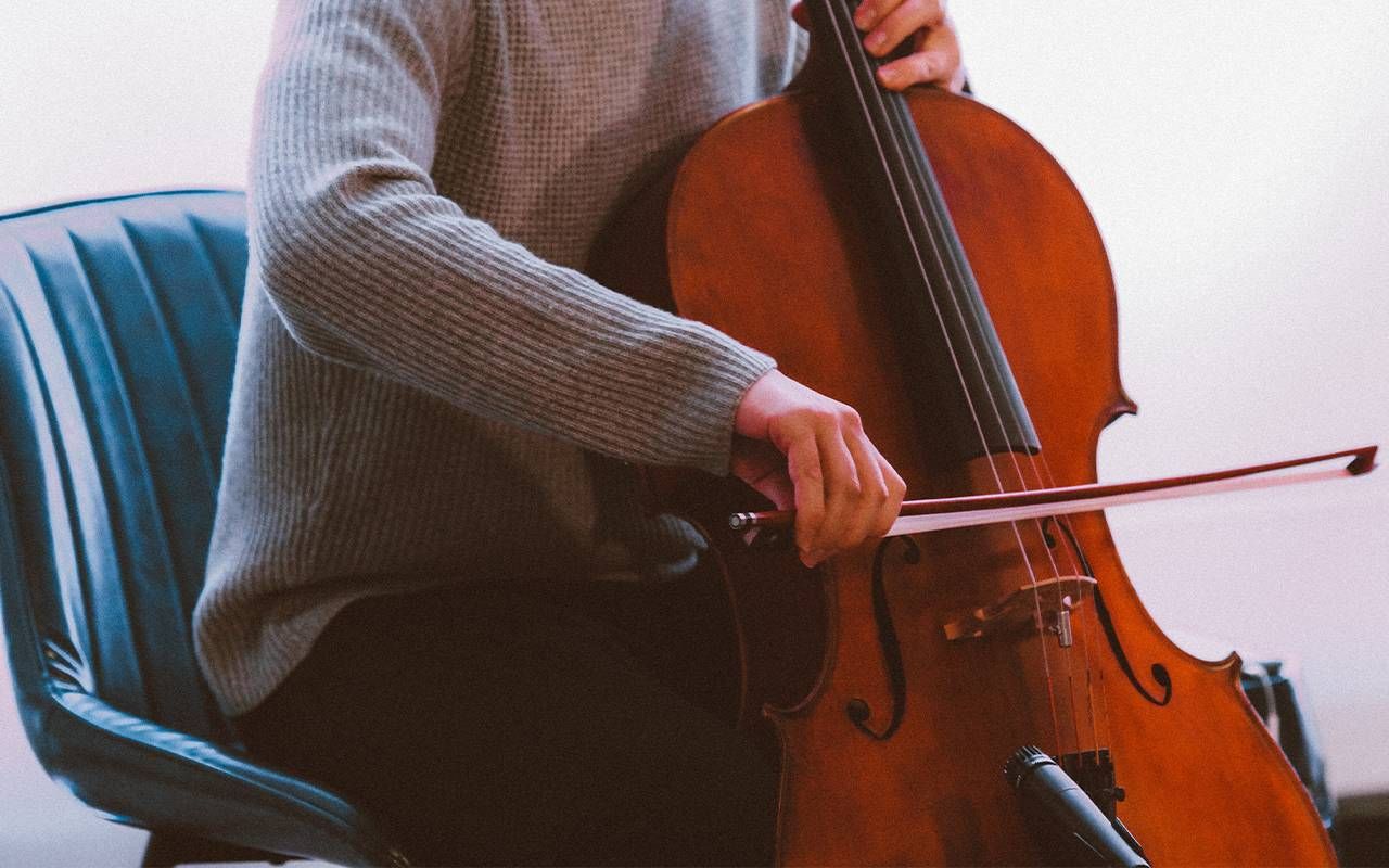 A man wearing a grey sweater practicing the cello. Next Avenue, decrease cognitive decline