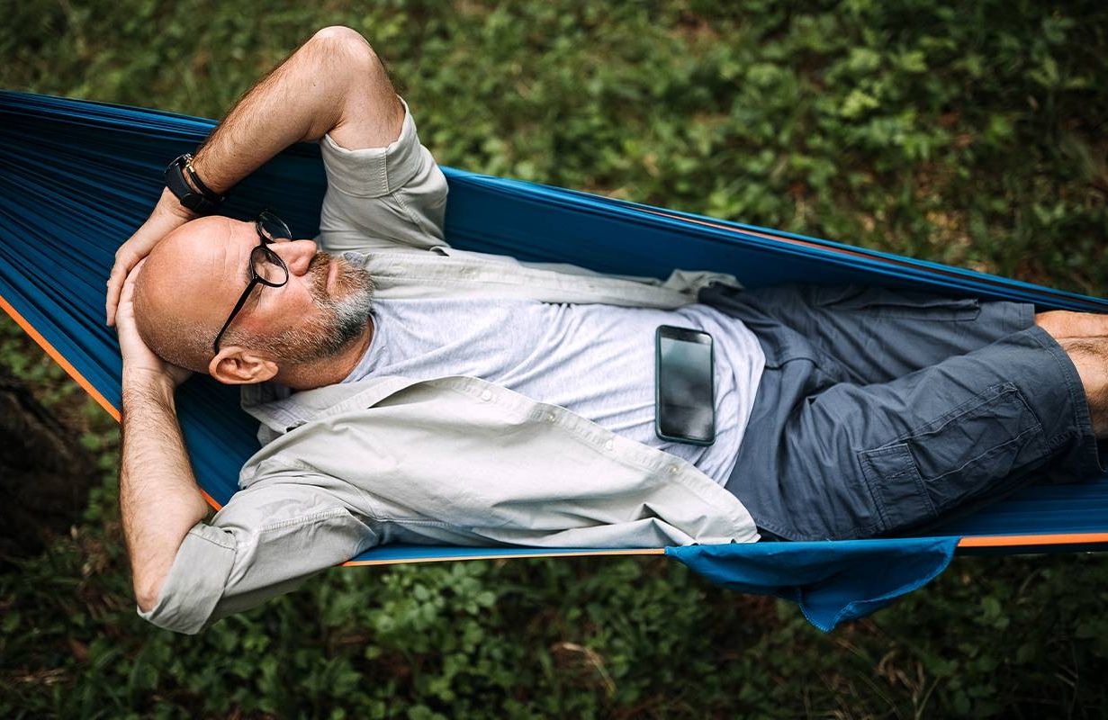 A man resting on a hammock ignoring his phone. Next Avenue