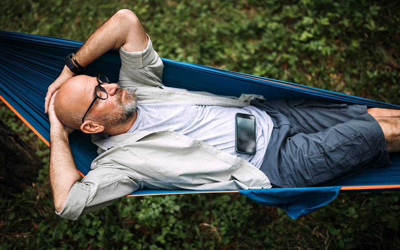 A man resting on a hammock ignoring his phone. Next Avenue
