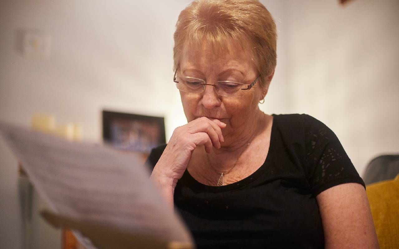 An older woman looking worried while paying her medical bills. Next Avenue, open enrollment, high medicare premiums