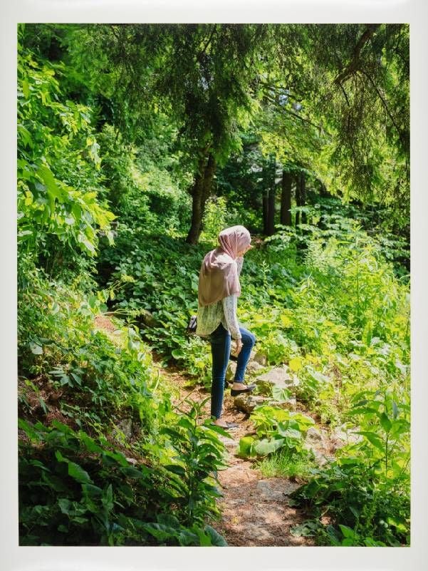 A photograph of a woman walking on a forested path. Next Avenue