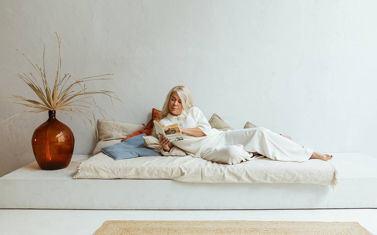 A woman laying down reading a book. Next Avenue, coastal grandma, adaptive furniture disabled adults