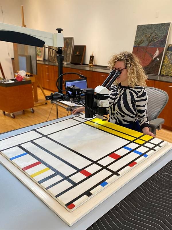 A museum conservator looking at a painting through a microscope. Next Avenue