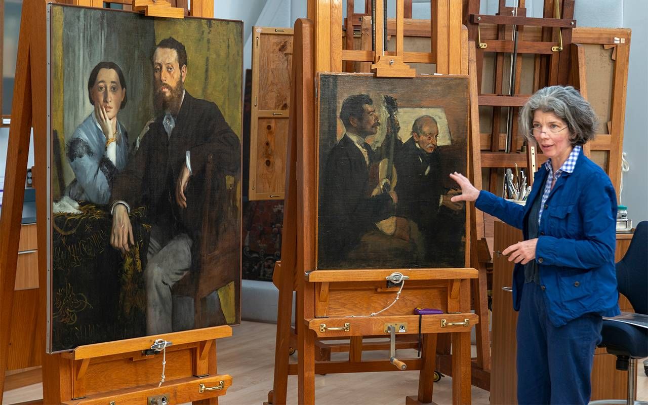 A museum conservator standing next to two paintings. Next Avenue